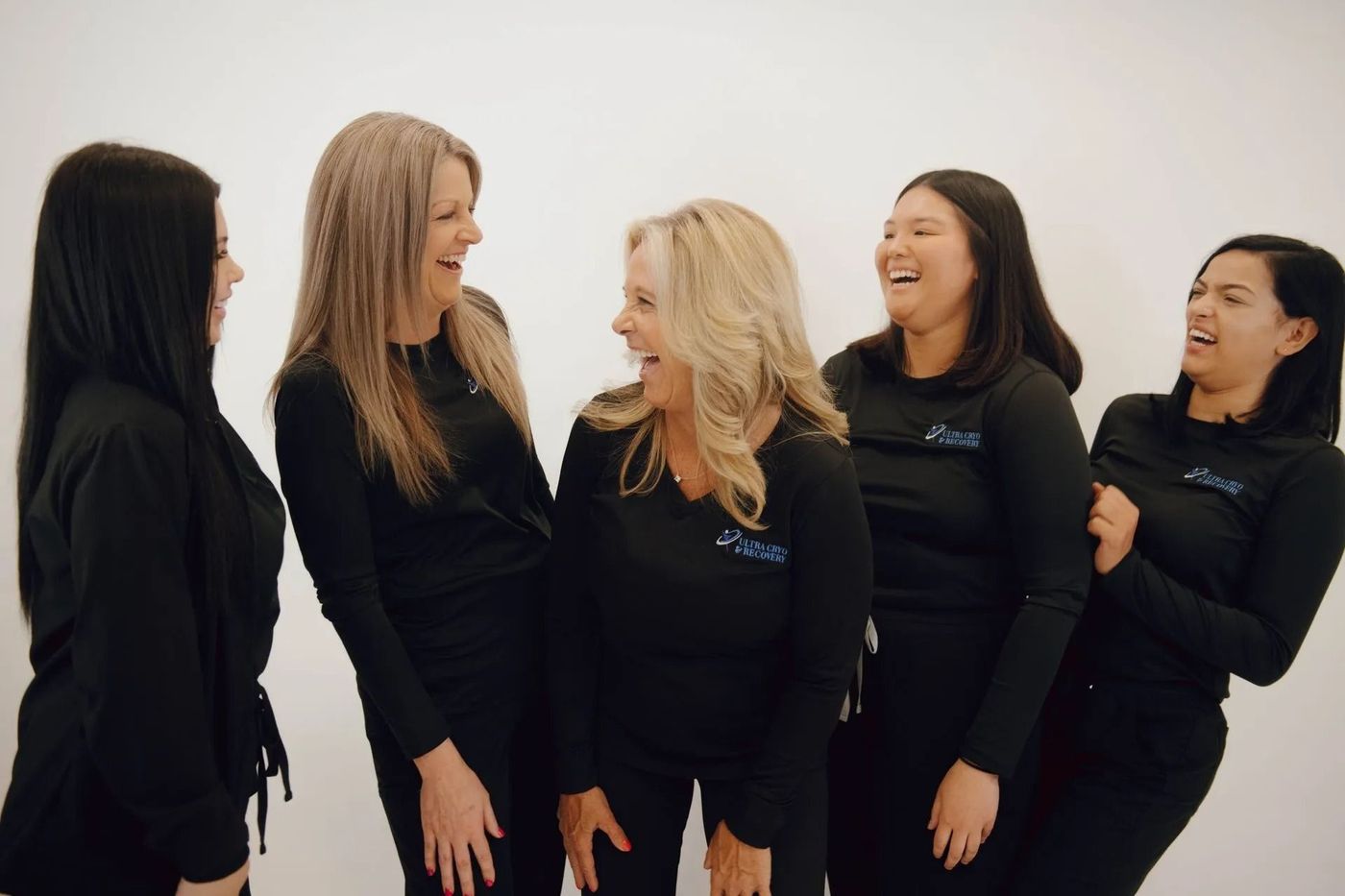 Five people in black shirts laugh against a white backdrop.