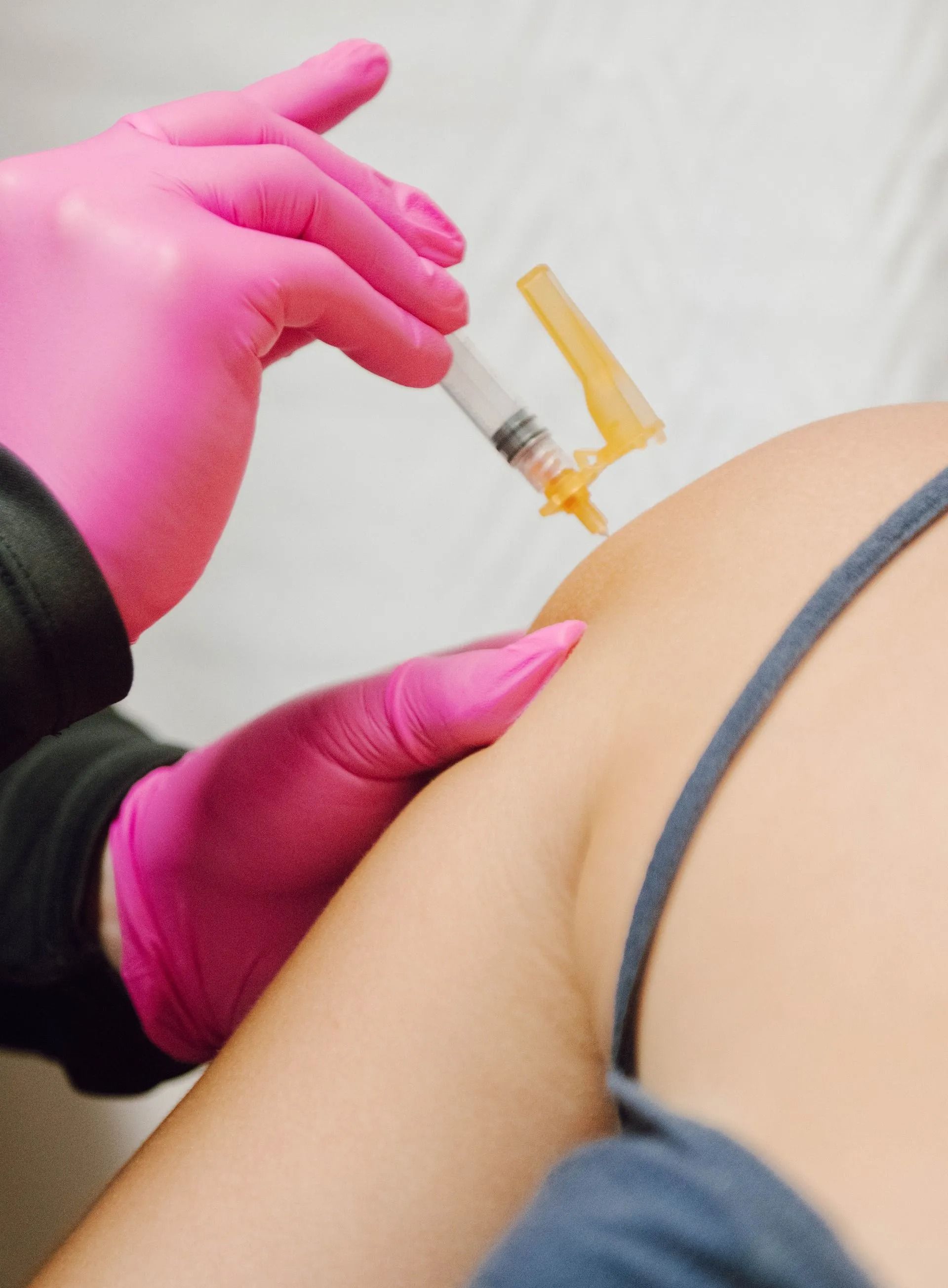 Person's arm receiving an injection. Pink gloved hand holds syringe against the upper arm.