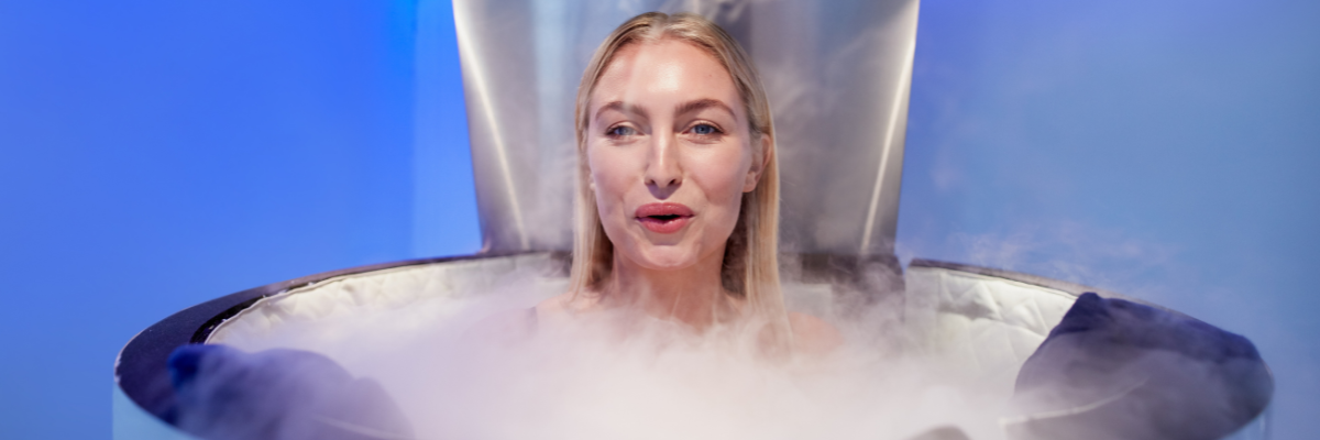 A person in a cryotherapy chamber, surrounded by fog. Blue and silver tones.