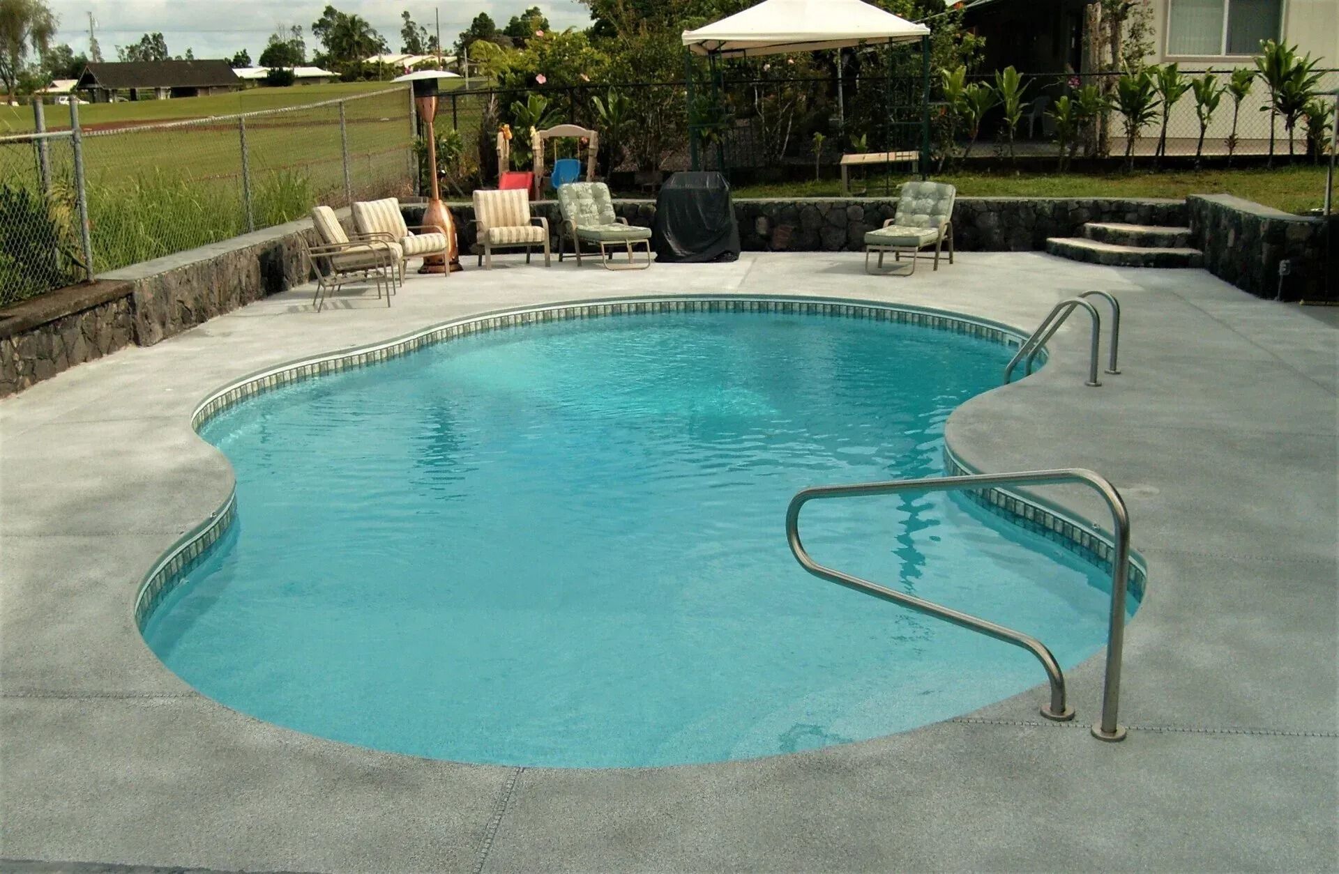 Backyard swimming pool with turquoise water, concrete deck, lounge chairs, and a patio umbrella