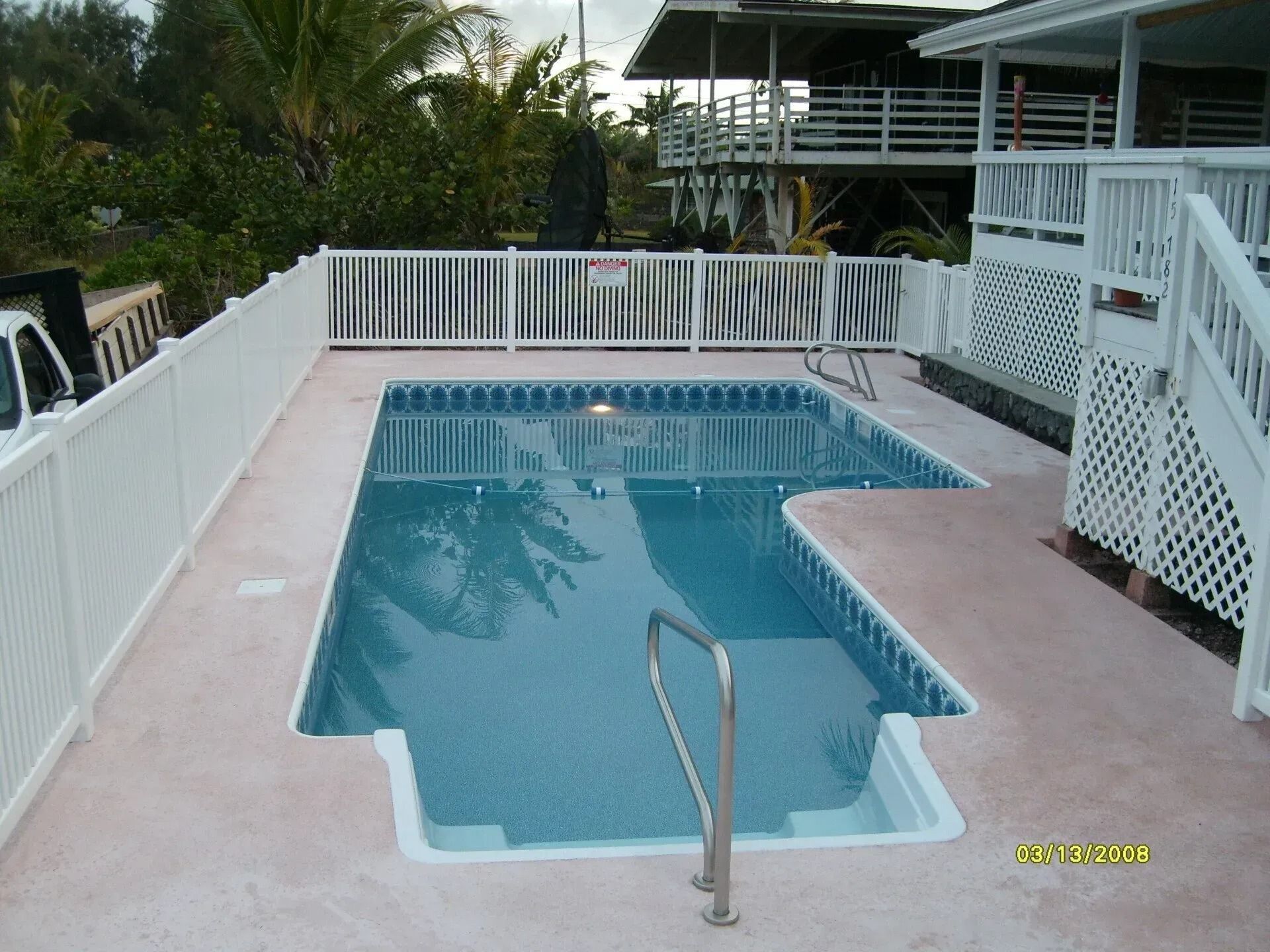 Backyard pool with blue water, white fence, and a metal handrail leading into the shallow end