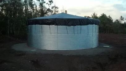 Large round metal water tank with a black cover, surrounded by trees at dusk