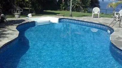 Blue swimming pool with curved edge beside a patio and lawn, with chairs in the background