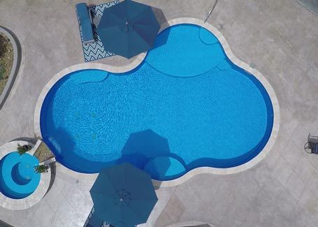 Aerial view of a blue, kidney-shaped swimming pool with surrounding patio and umbrellas.