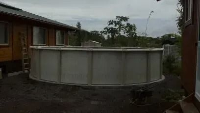 Backyard with a large round above-ground pool between two wooden houses on a cloudy day
