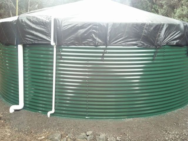 Green corrugated water tank with black cover and white pipes outdoors