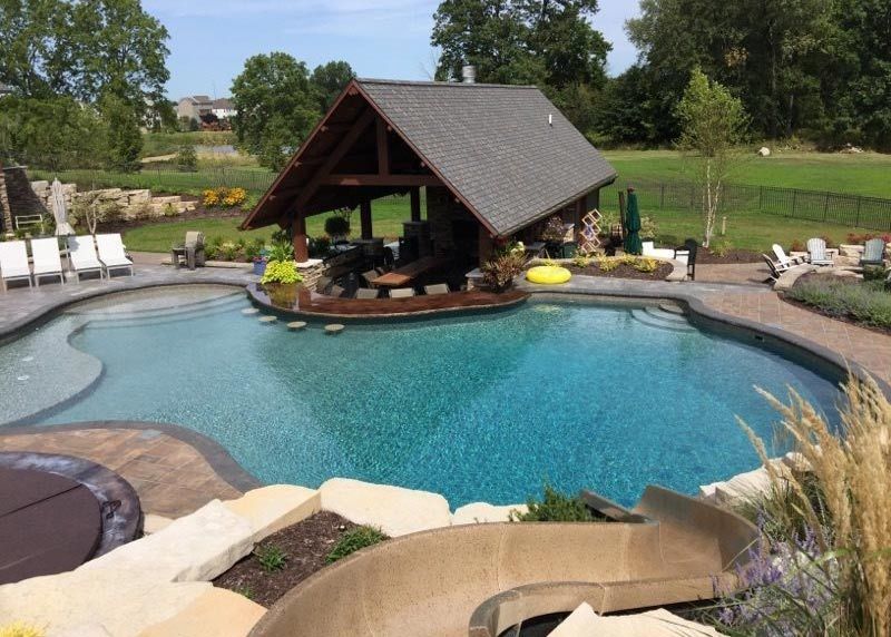Backyard pool with a thatched-roof cabana, stone deck, and lounge chairs surrounded by greenery