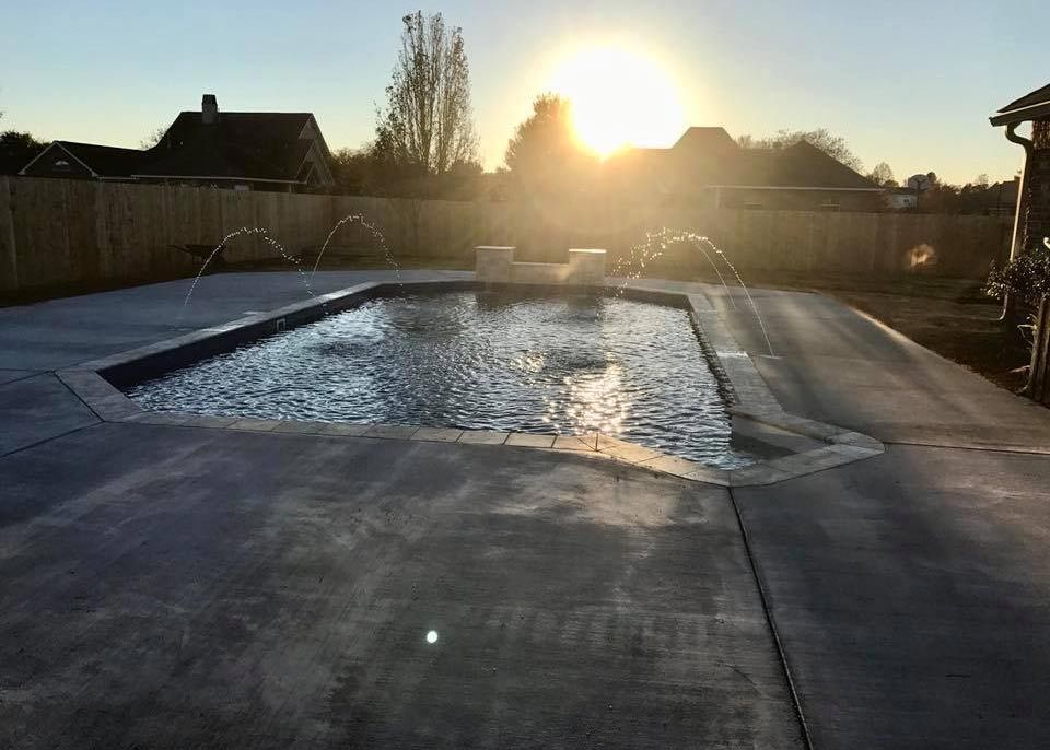 Outdoor swimming pool at sunset with water reflecting the low sun and houses in the background