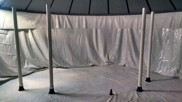 Indoor space with white tarp-covered walls and floor, showing several vertical metal poles arranged in a room.