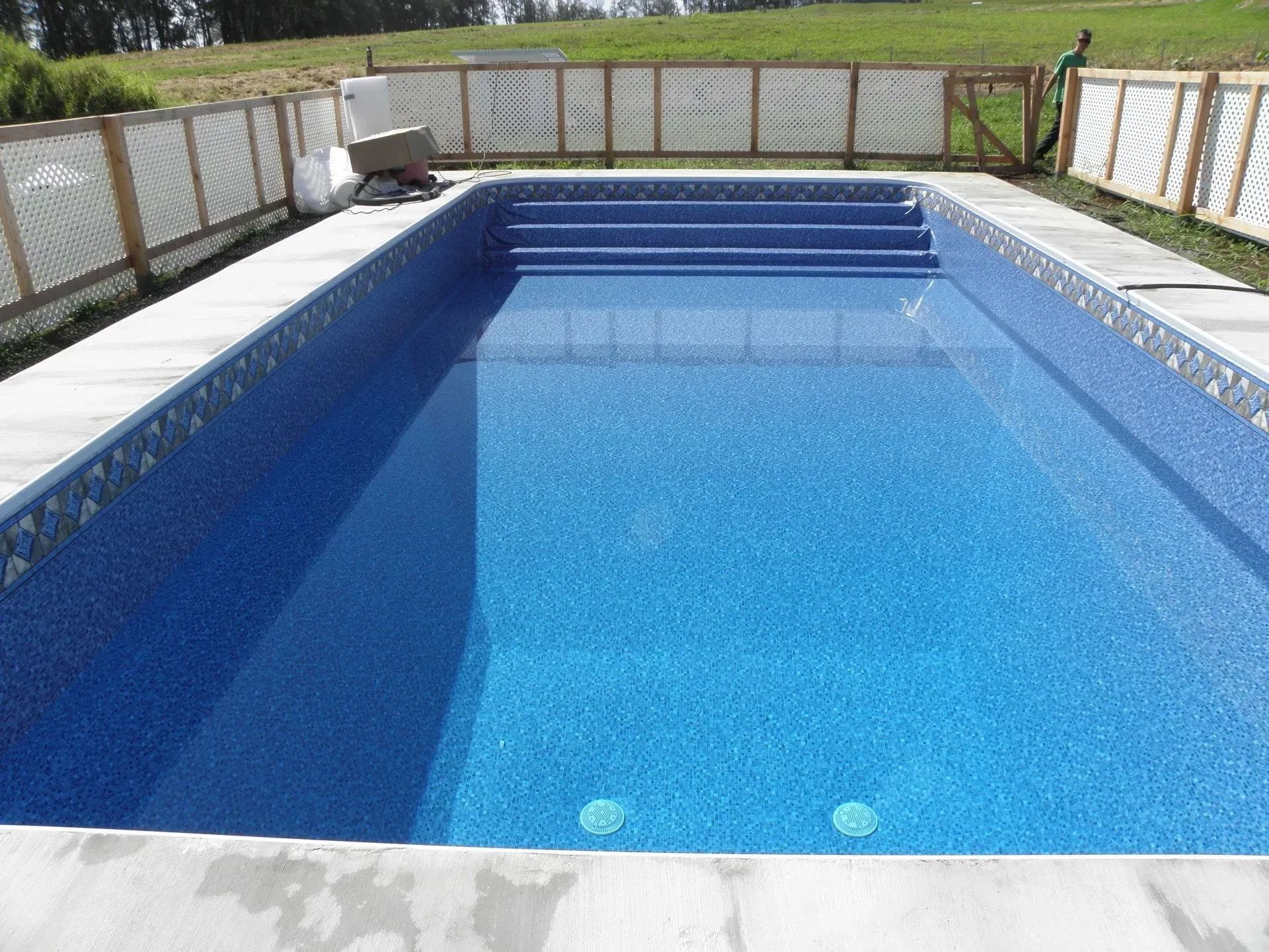 Backyard swimming pool with blue water, white deck, and wooden fence surrounding it