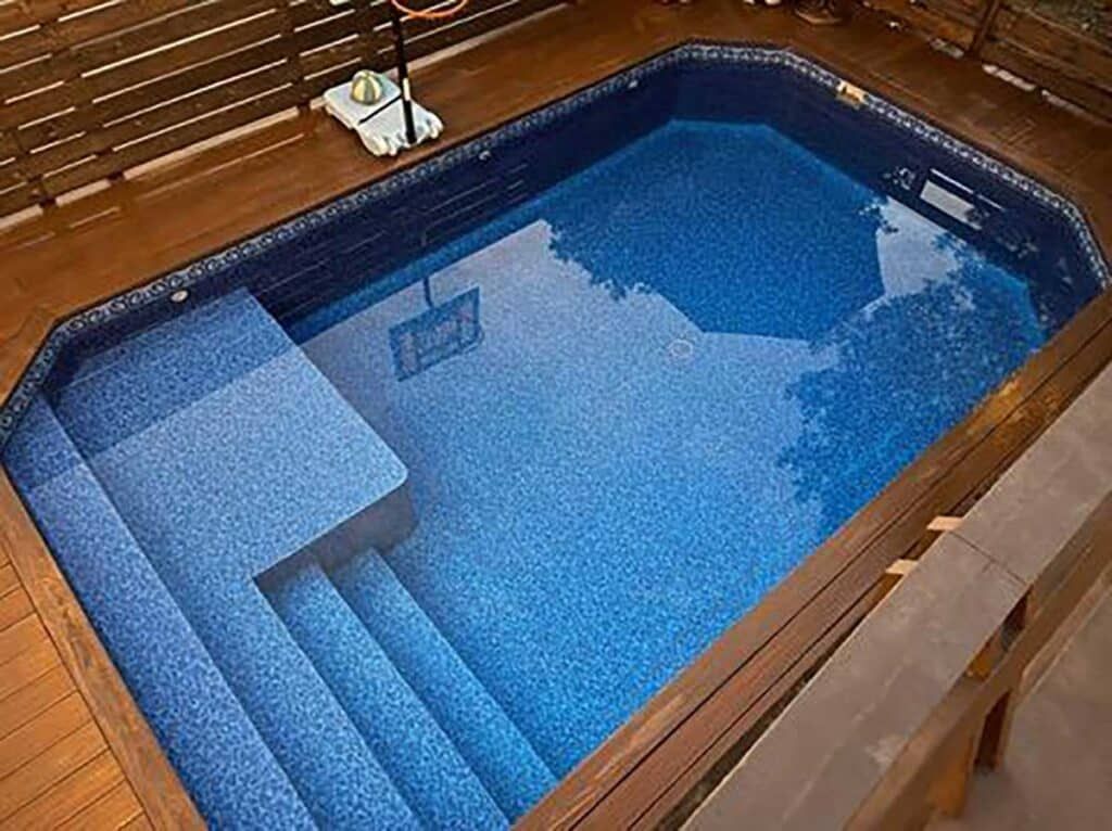 Small indoor pool with blue water, wooden deck, and a partially submerged lounge chair
