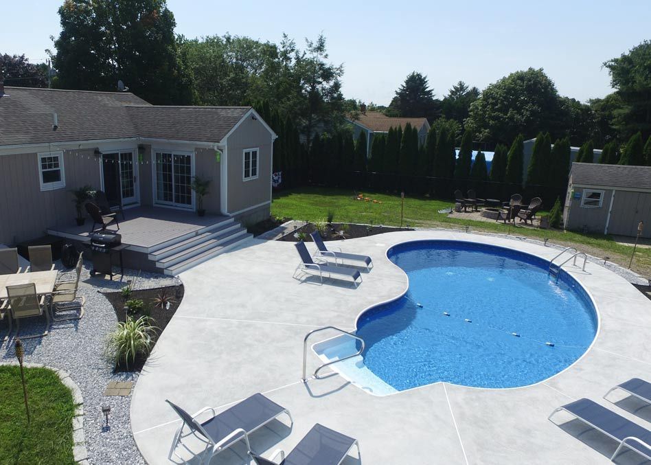 Backyard with a kidney-shaped blue pool, white patio, lounge chairs, and a house in the background