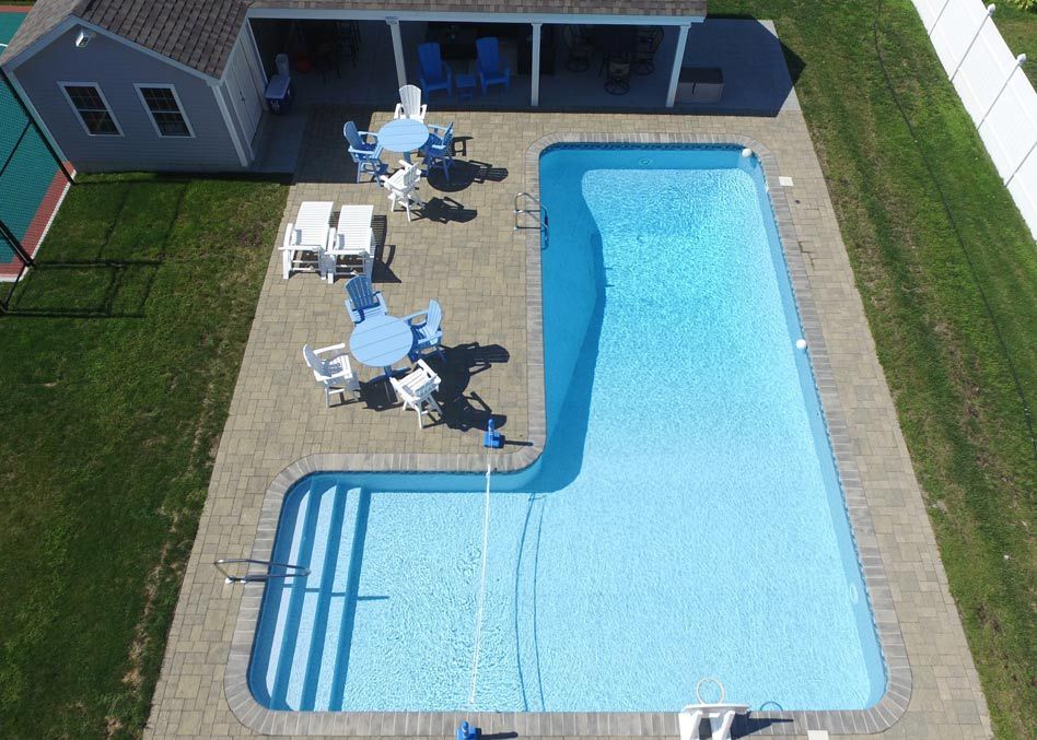 Backyard pool with blue water, patio tables and chairs, and a house in the background