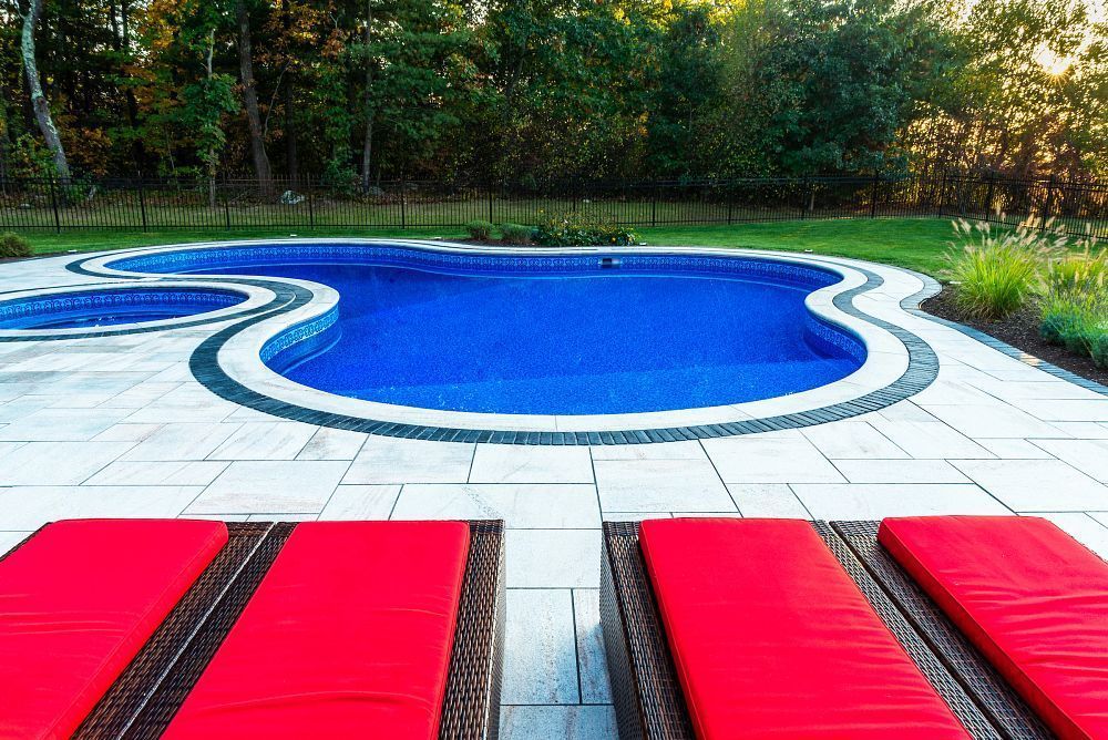 Blue swimming pool with curving edge, white deck, and red lounge chairs in a sunny backyard
