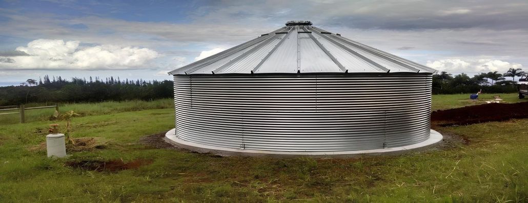 Small corrugated metal water tank in a grassy field under a cloudy sky