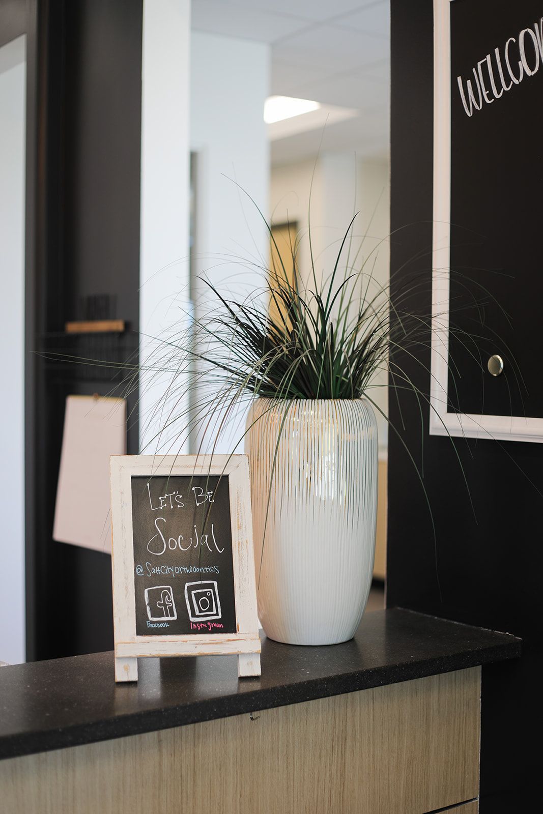 A chalkboard is sitting on a counter next to a potted plant.