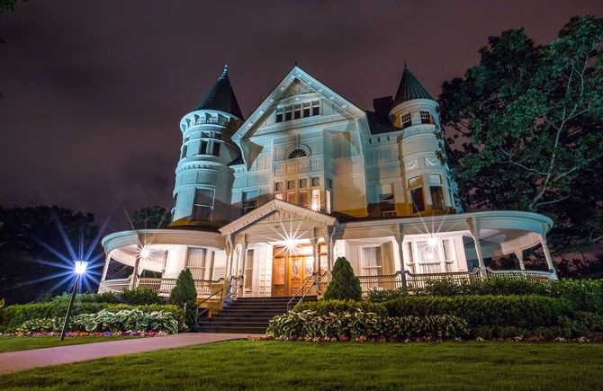 A large white house with a porch is lit up at night.