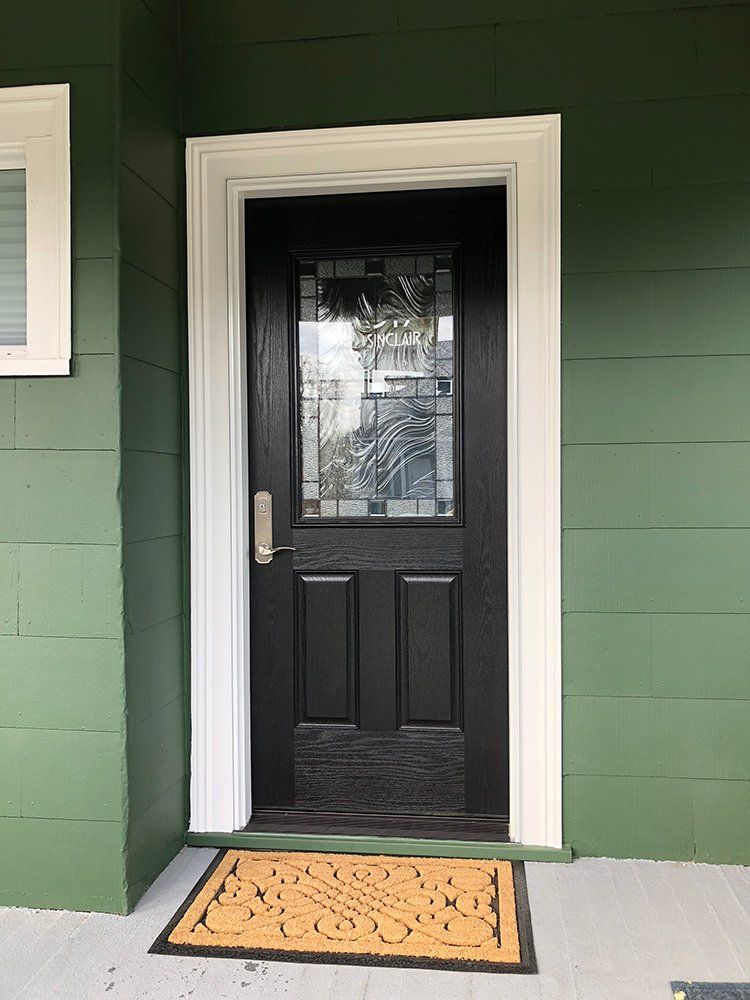 A black door with a stained glass window is on a green house