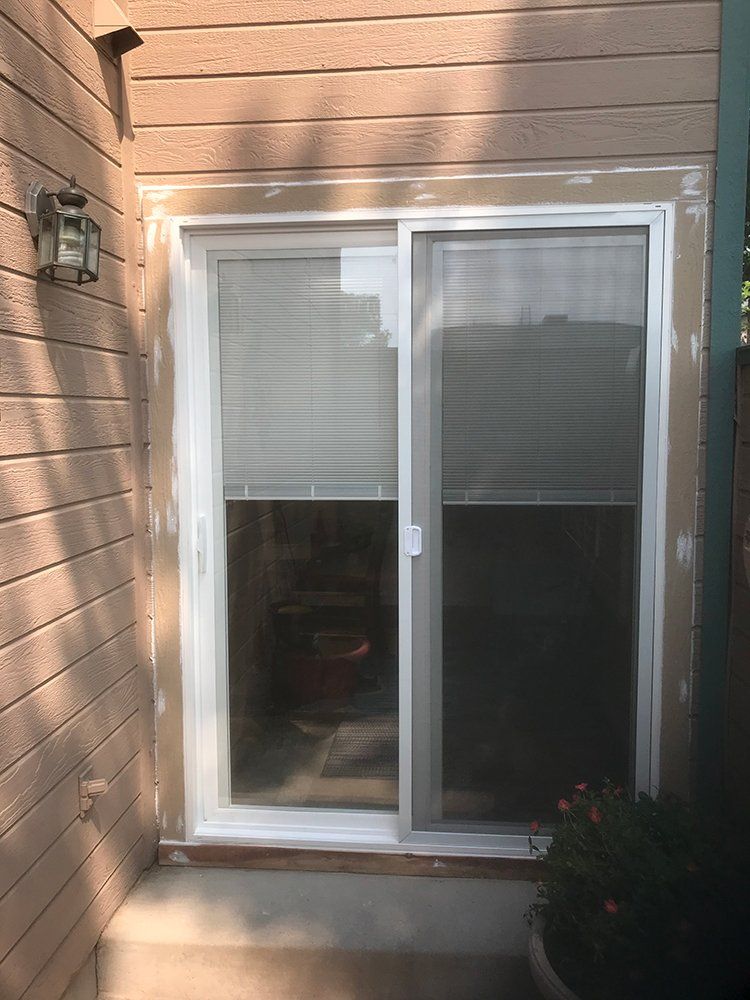 A sliding glass door with blinds on it is sitting on the side of a building