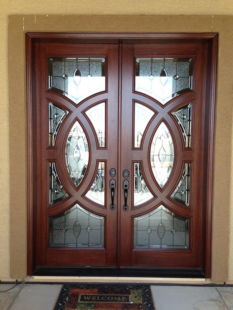 A pair of wooden doors with stained glass and a welcome mat