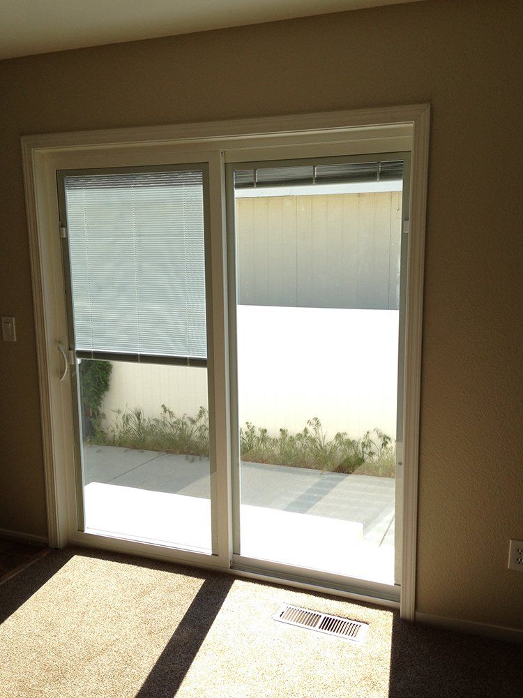 An empty room with a sliding glass door and blinds