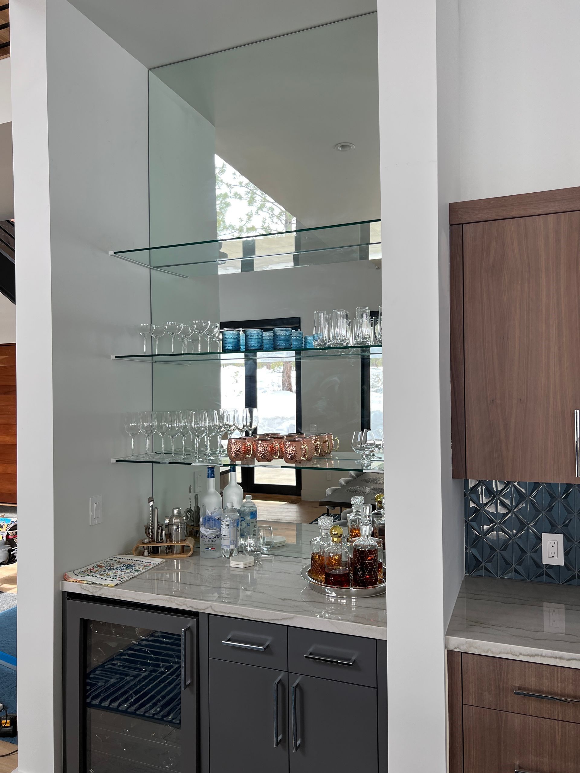A kitchen with a bar and glass shelves filled with bottles and glasses