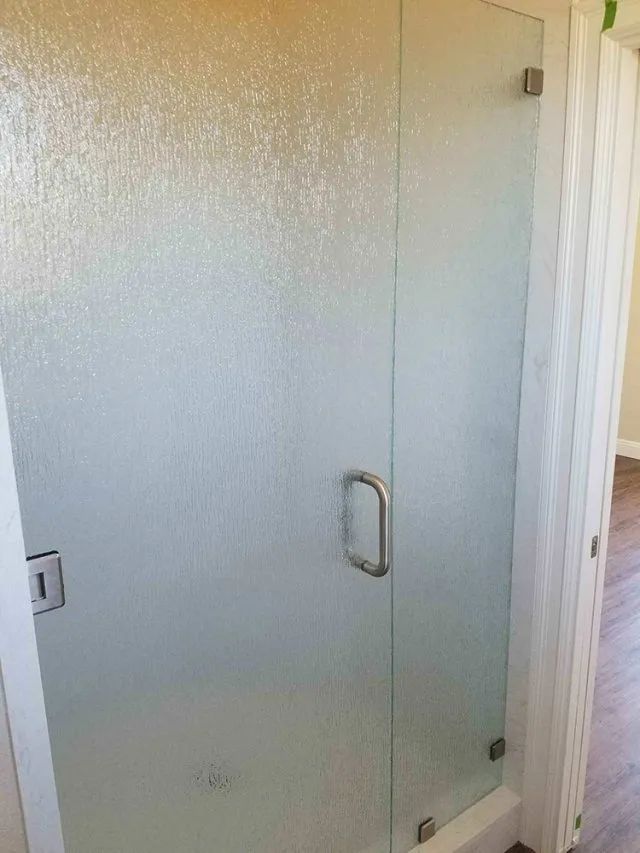 A glass shower enclosure with a stainless steel handle on the door