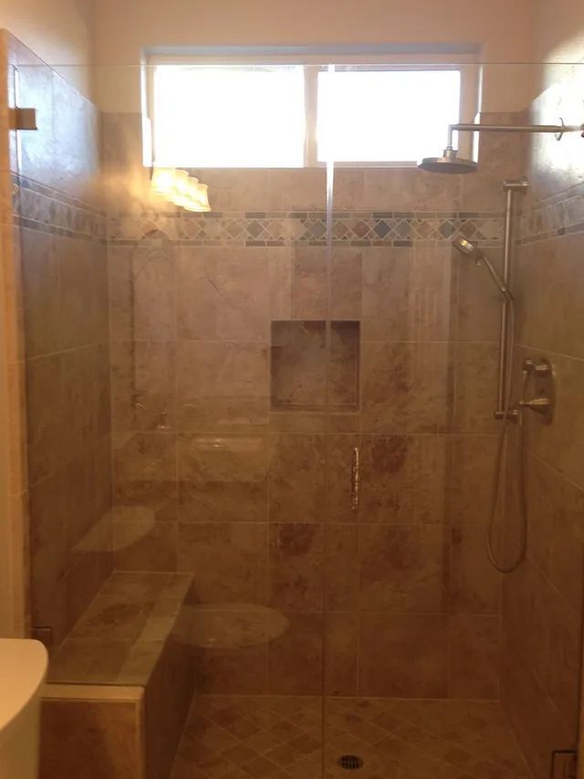 A bathroom shower with a glass door and a window