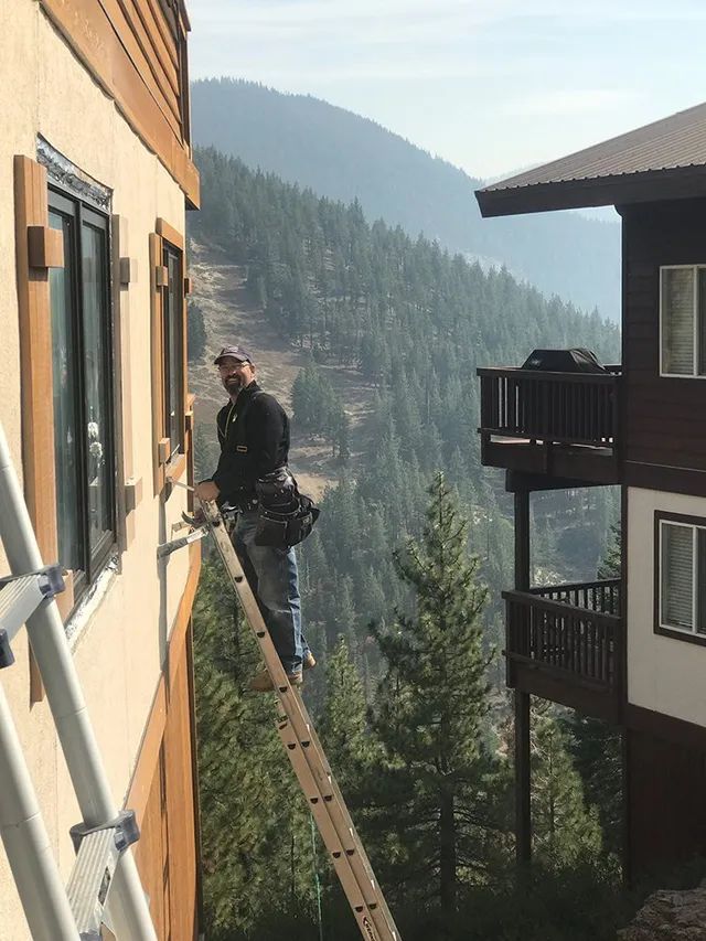 A man is standing on a ladder on the side of a building installing a window