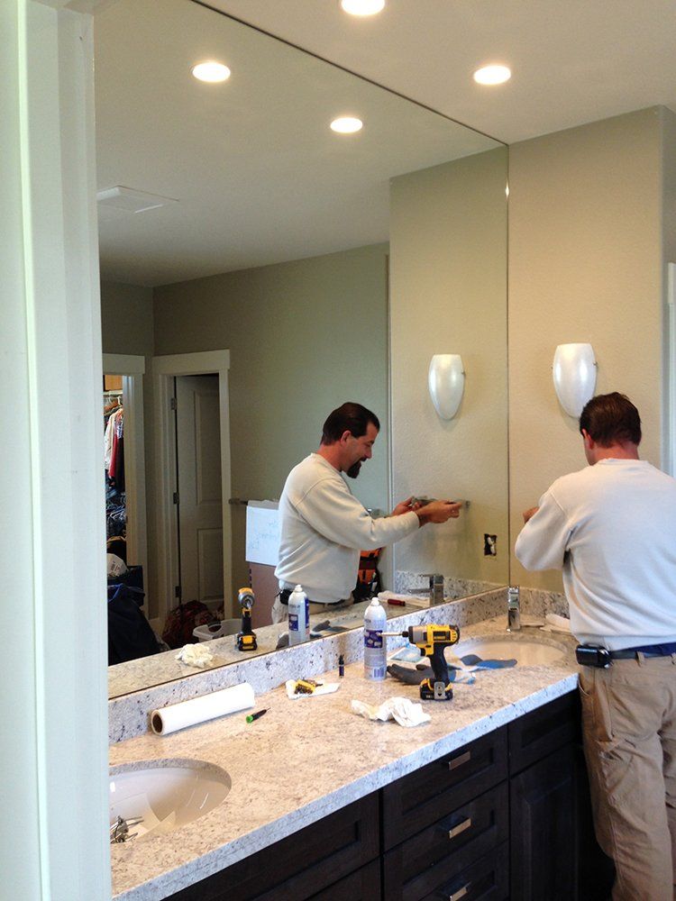A man is installing a large mirror in a bathroom