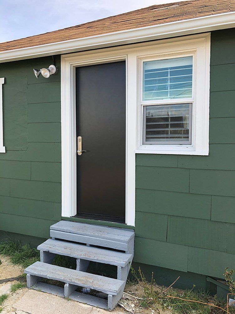 A green house with a black door and steps leading to it