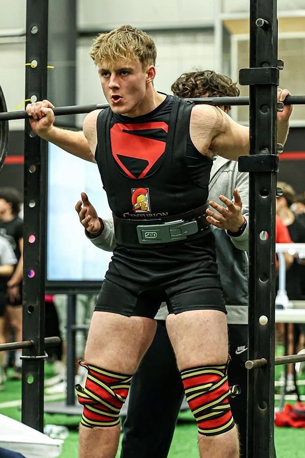 A young man is squatting with a barbell in a gym.