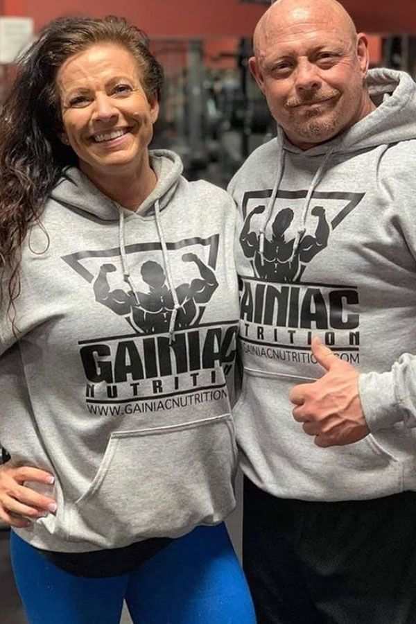 A man and a woman are standing next to each other in a gym wearing hoodies.