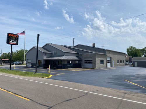 Small gray roadside building with a parking lot and sign under a blue sky