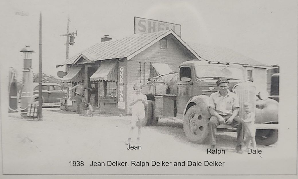 Two men by a gas station; truck parked at pump beside a small building and sign.