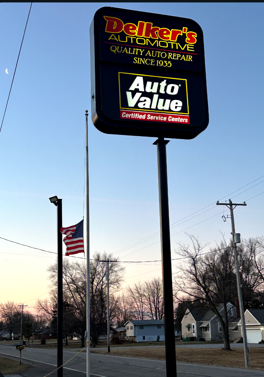 Auto Value and Delker’s Automotive sign beside an American flag at dusk