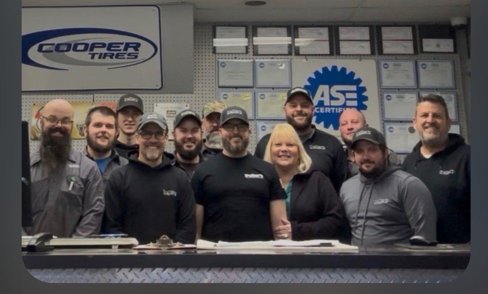 Auto shop staff posing behind a counter, with Cooper Tires and ASE signs in the background.
