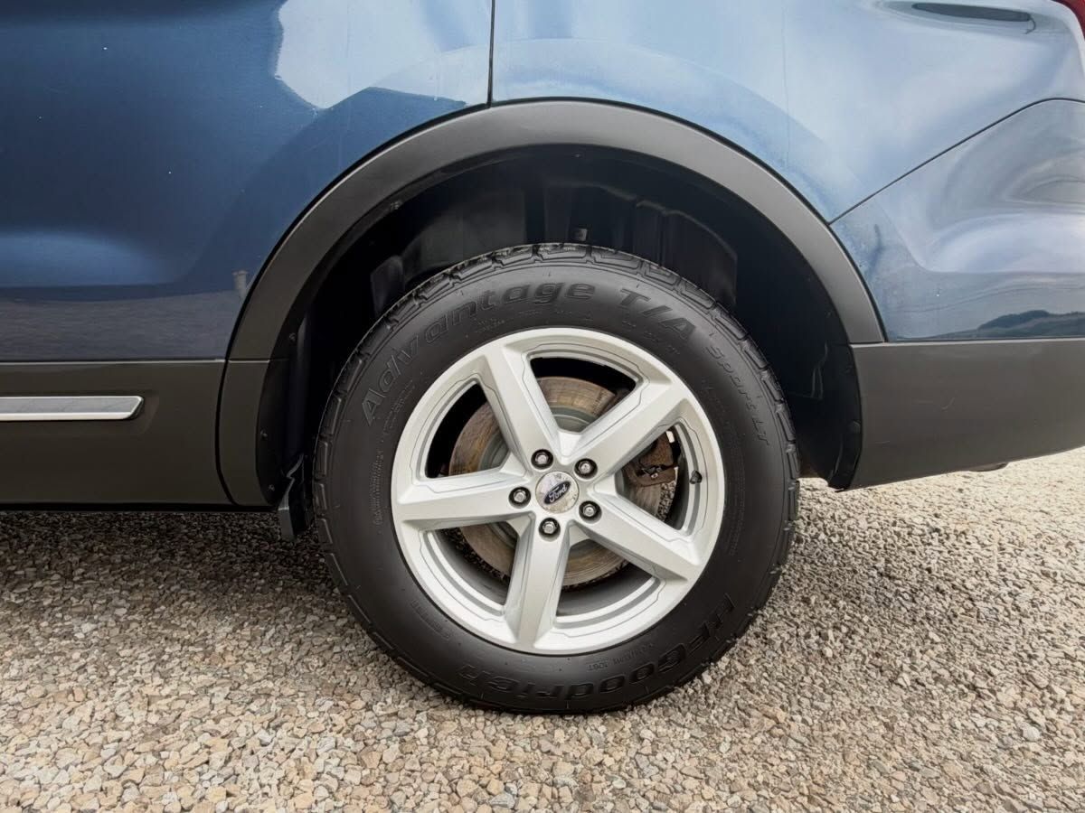 Close-up of a blue car’s rear wheel and fender on a gravel surface.