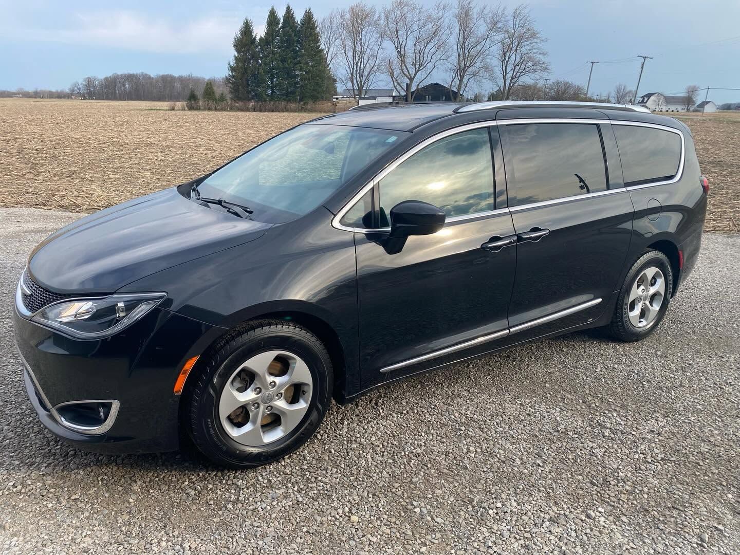 Dark gray minivan parked on a gravel road beside a field under a cloudy sky