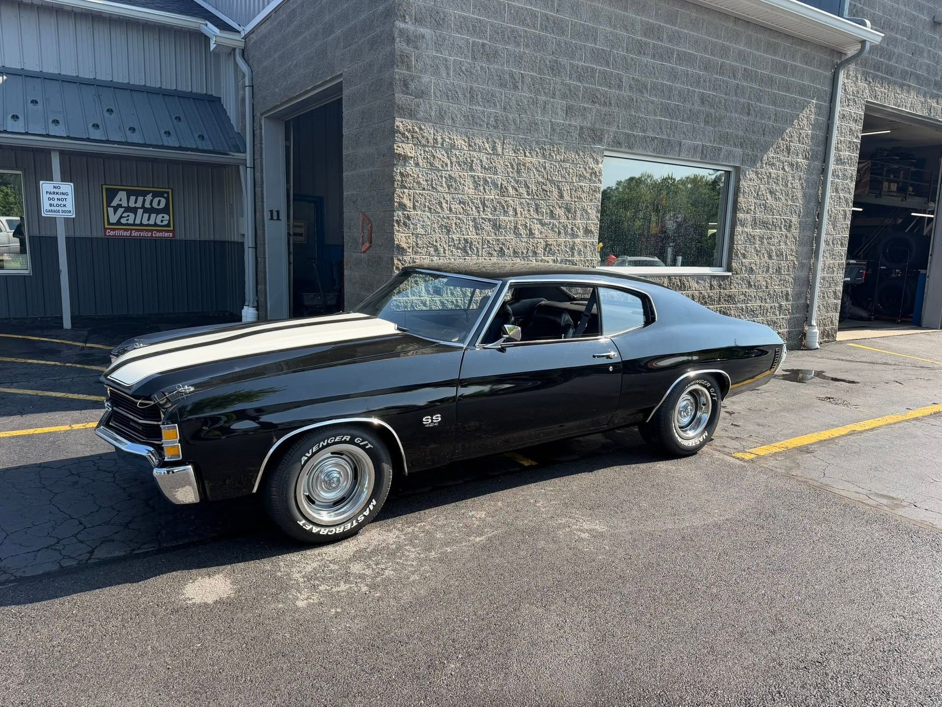 Black classic muscle car parked outside a stone building with a sign and open window.