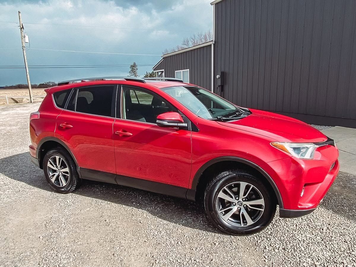 Red SUV parked on gravel beside a gray building under a cloudy sky