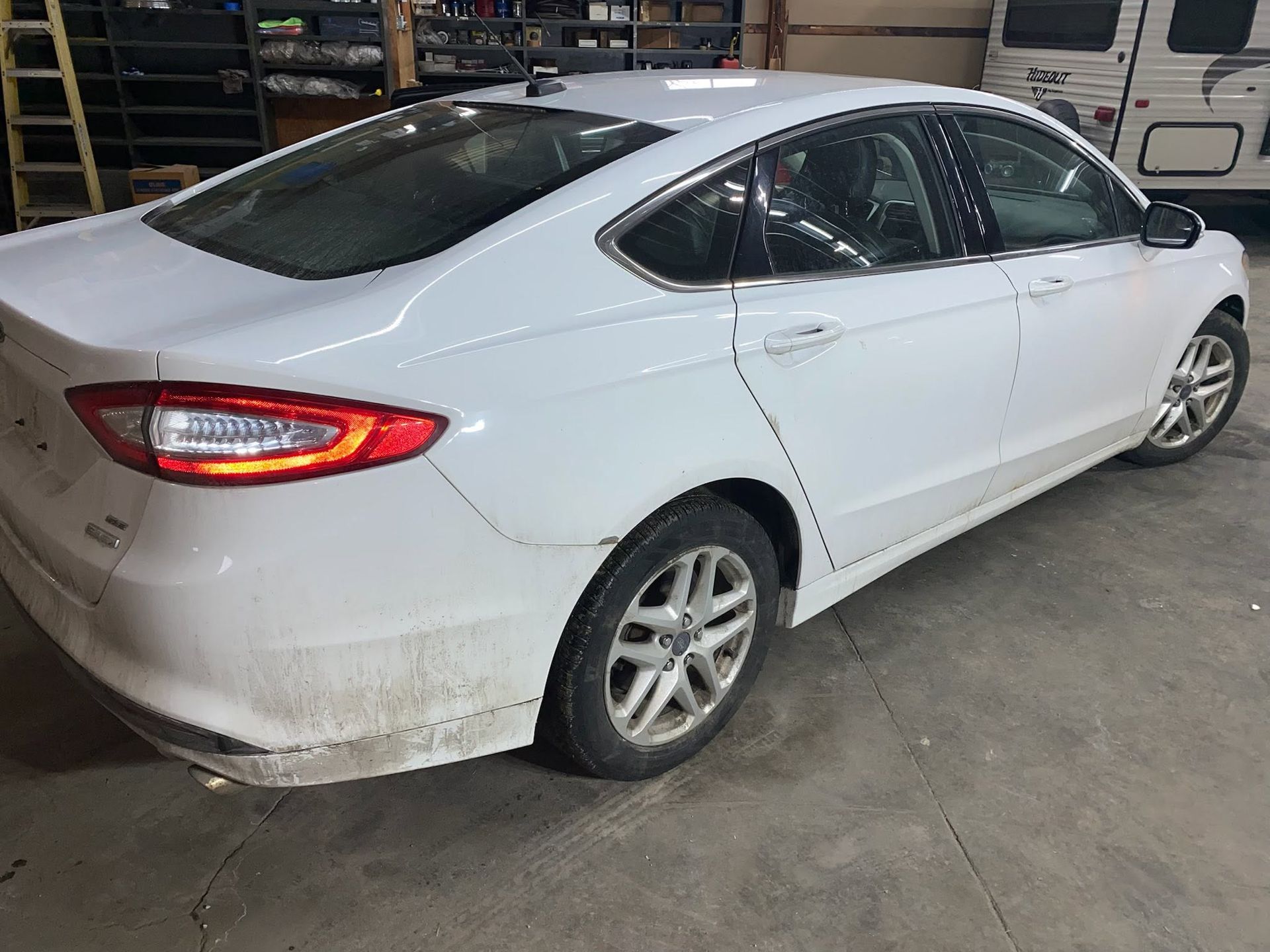 White sedan parked indoors with dirty lower panels and rear quarter view