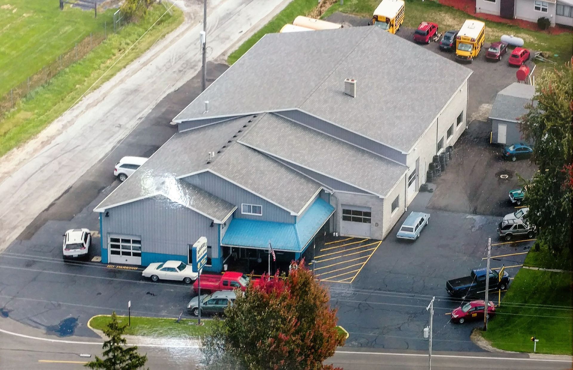 Aerial view of a blue commercial building with parked vehicles and a driveway near a grassy roadside