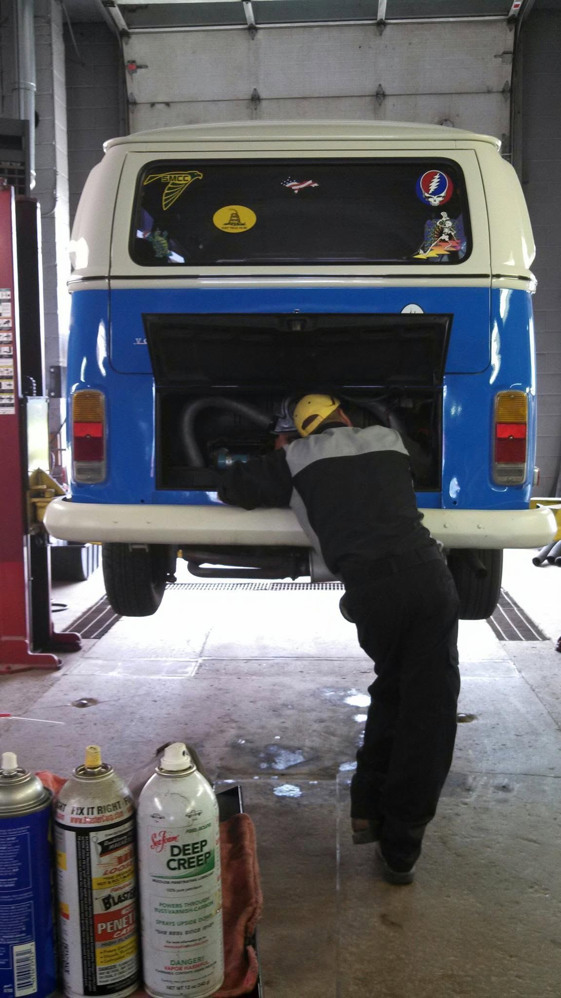 Person leaning into the back of a white van in a garage, with gas cylinders in the foreground.