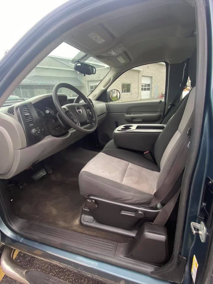 Car interior with gray front seats and steering wheel, viewed from the open driver’s door