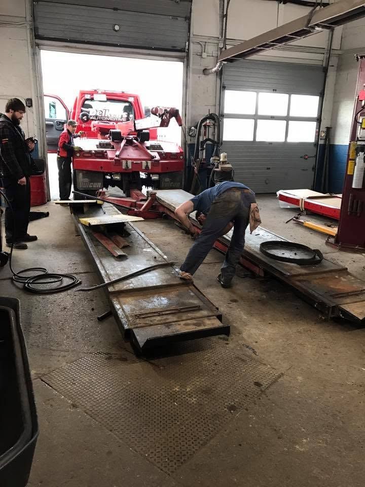 Auto body shop with workers aligning a red vehicle frame on long metal ramps
