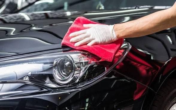 Person wiping a black car’s headlight and hood with a red cloth during car detailing