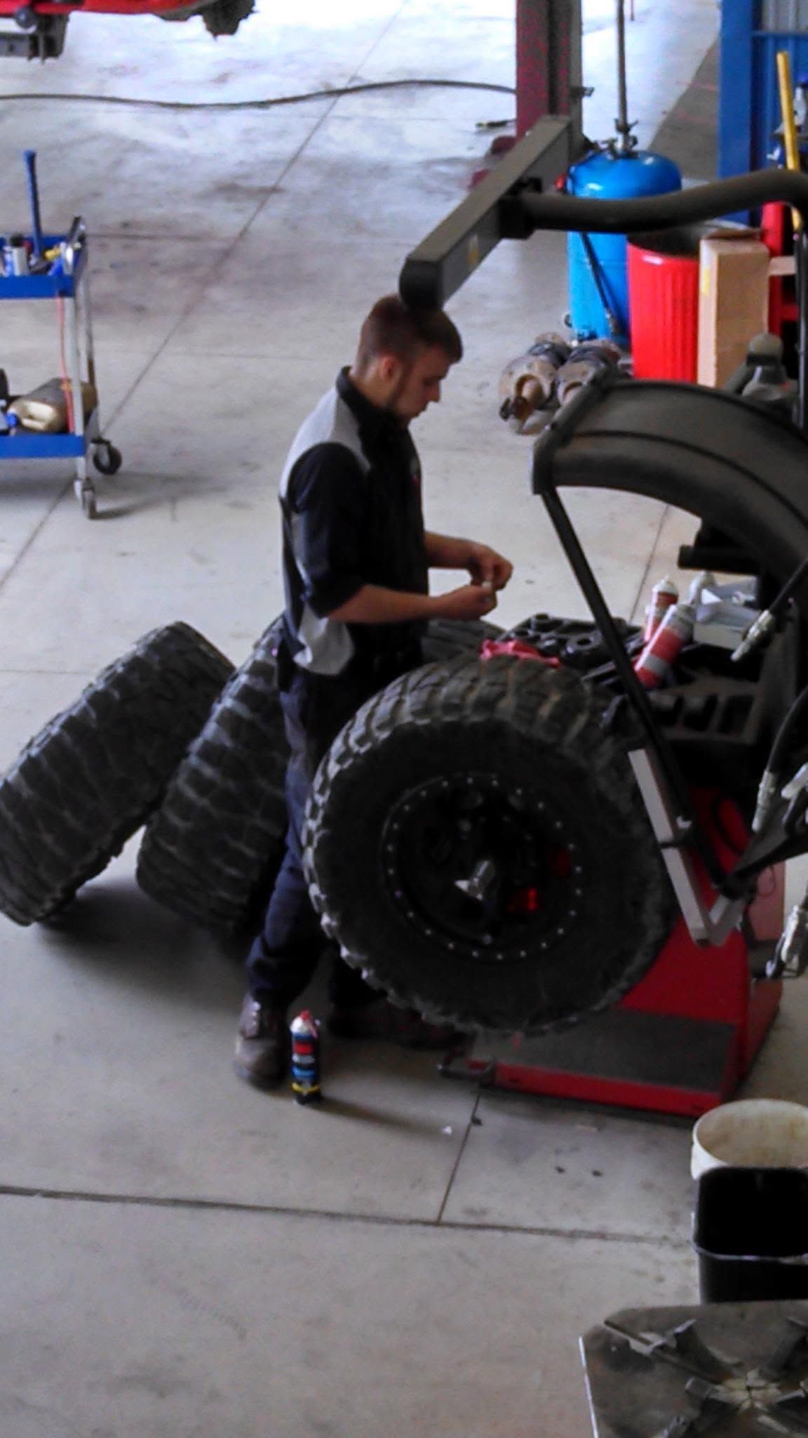 Mechanic working on a large tire beside a vehicle in a garage.