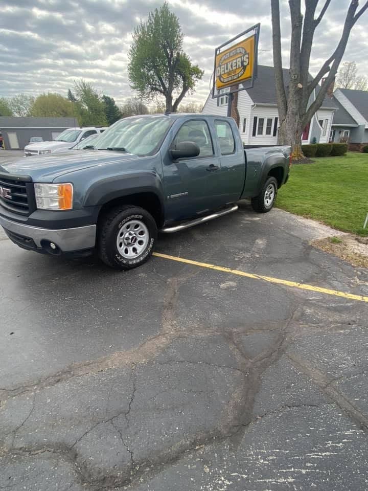 Gray pickup truck parked in a lot beside a road sign and grassy lawn under cloudy skies