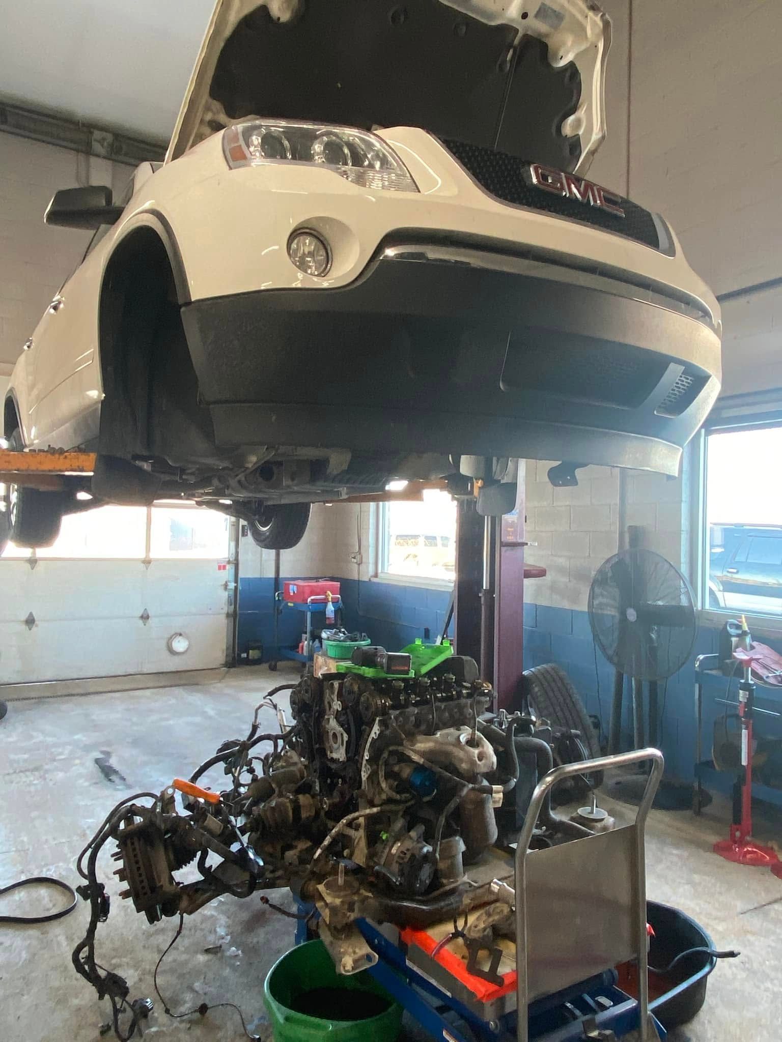 Car suspended in a workshop over a partly disassembled engine and frame on a lift